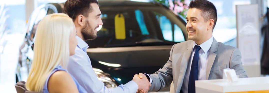 Young couple shaking hands with car salesman