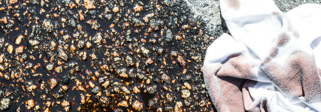 An oil spill on a driveway with a dirty rag sitting next to it
