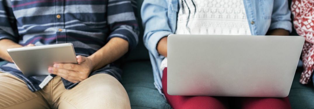 Two people sitting on a couch looking at their tablet and computer