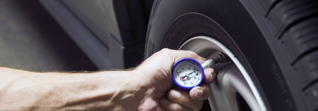 Someone checking their tire pressure with a hand-held tire gauge