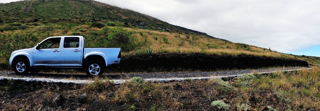 Pickup truck driving next to grassy mountain