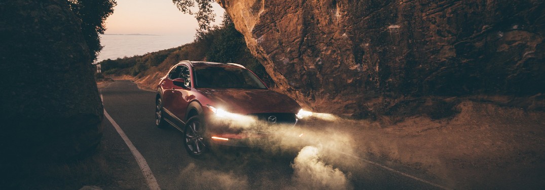 A red 2020 Mazda CX-30 driving between two large rocks in a foggy atmosphere.