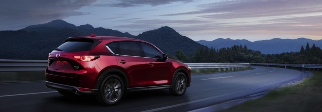 A red 2021 Mazda CX-5 driving down a road in the evening.