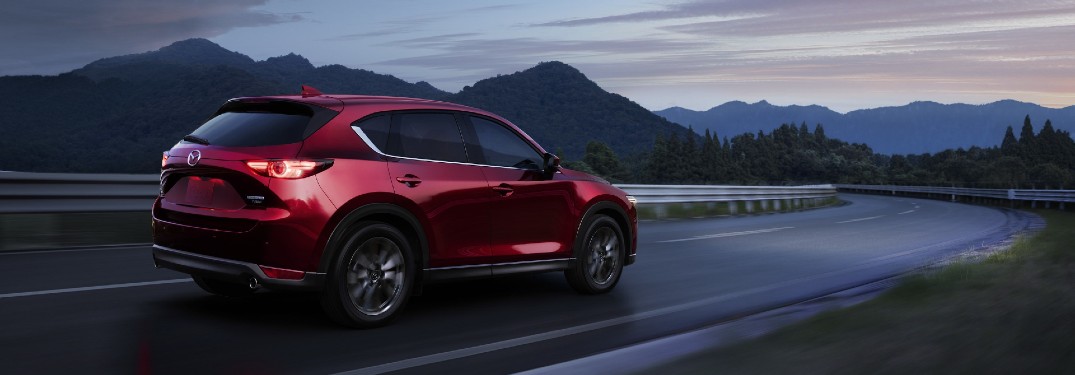 The rear and side view of a red 2021 Mazda CX-5 driving on an open road at dusk.