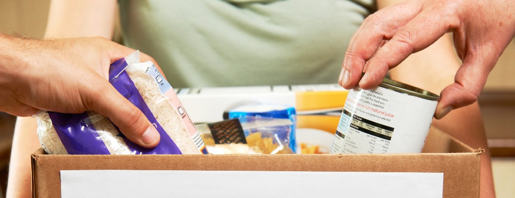 A group of people placing non-perishable items on a donation box.