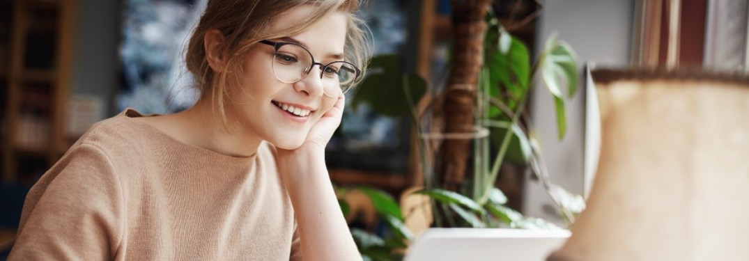 A young woman looking at a laptop and smiling.