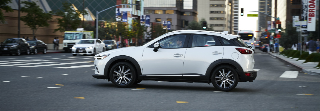 side view of white 2018 mazda cx-3 driving through intersection of downtown city