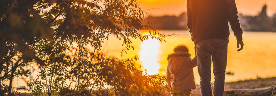Father walking with child in front of sunset