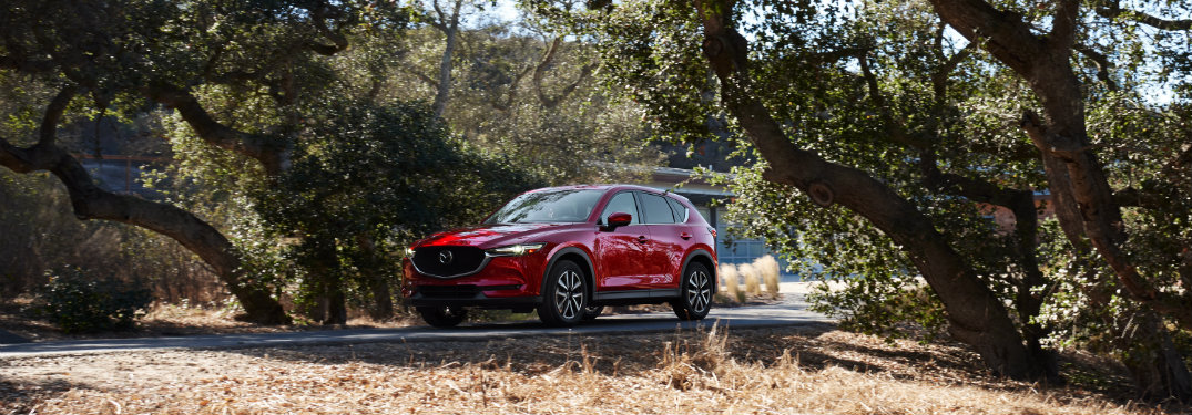 Long view of red 2018 Mazda CX-5 driving on tree-lined street