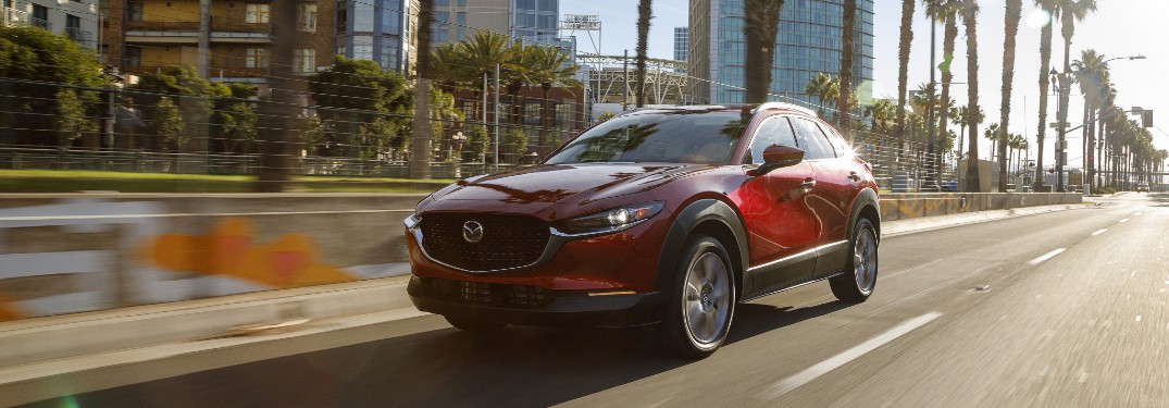 A red 2020 Mazda CX-30 driving quickly down an open city road.