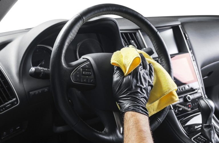 A steering wheel inside of a vehicle vehicle being cleaned by someone with a yellow rag.