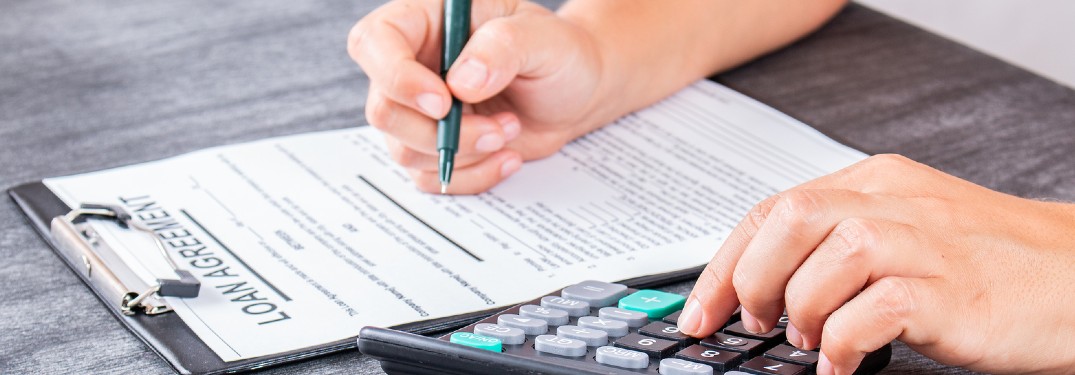 A person signing a contract with a calculator in their left hand.