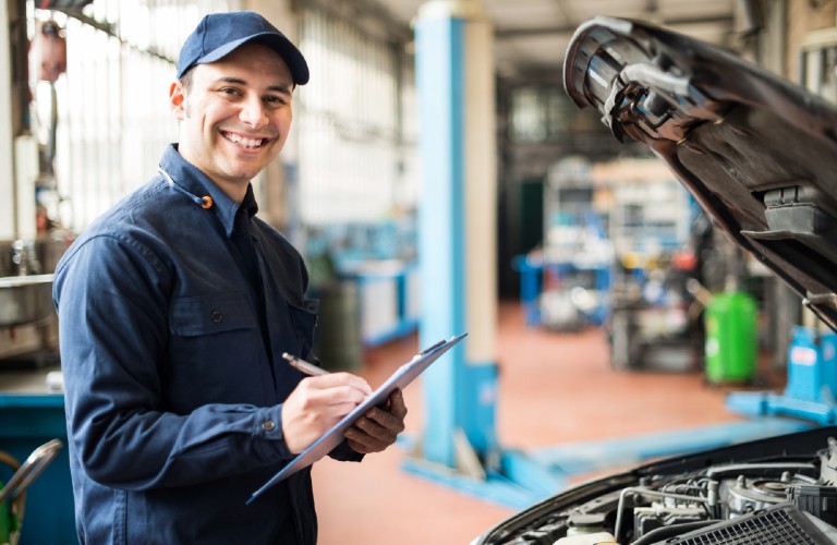 A service mechanic smiling while doing a checklist for a vehicle.