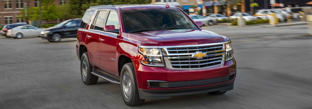 red 2018 chevrolet tahoe driving through parking lot in downtown area