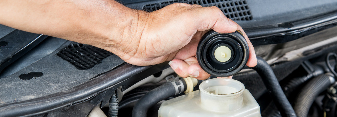 man checking brake fluid levels in car underneath hood