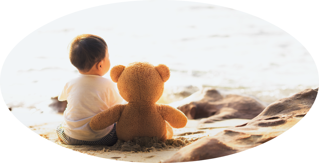 Little boy at the beach looking at the ocean with his teddy bear