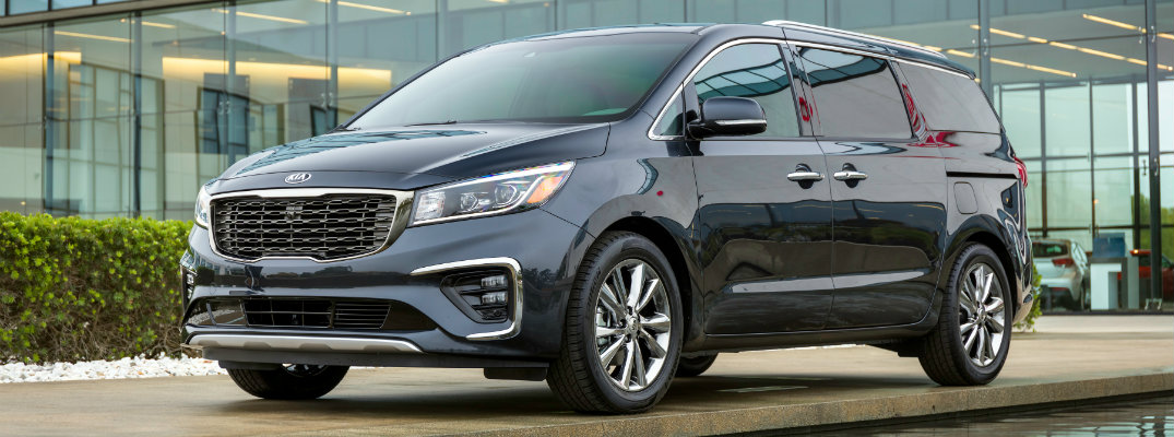 2019 Kia Sedona exterior shot parked outside a fancy glass paneled house next to a luxury pool