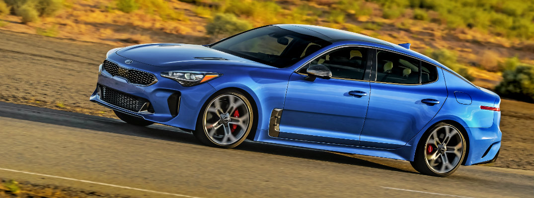 2018 Kia Stinger exterior shot angle blue paint color driving through a barren grassy wilderness