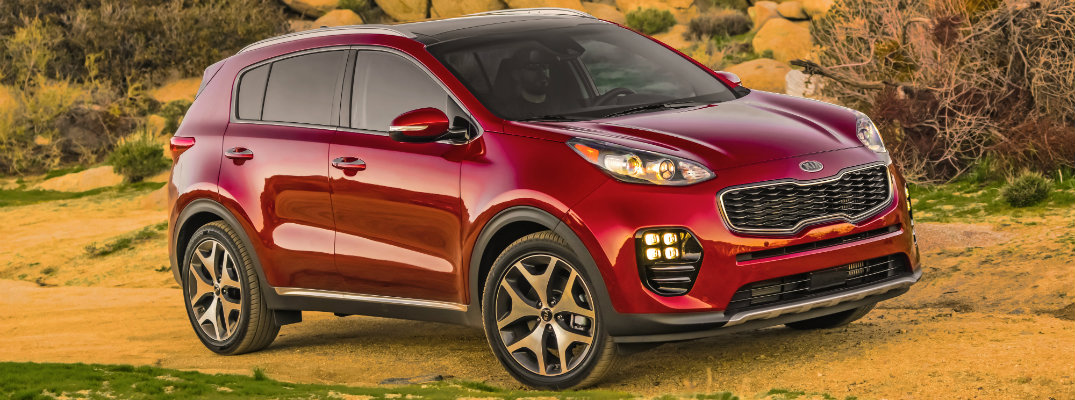 2019 Kia Sportage exterior shot hyper red paint job parked next to a rocky beach formation with a cloudy sky