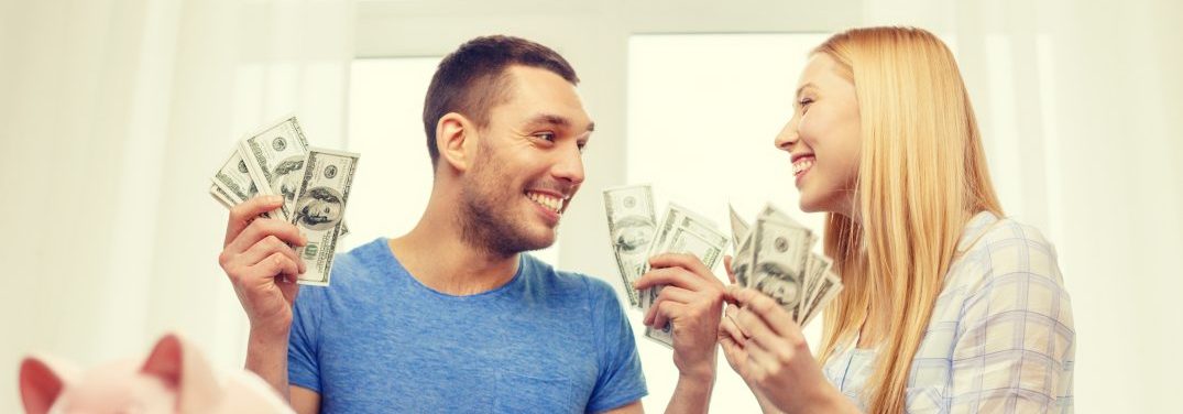 Man and woman sitting in a room holding hundred dollar bills looking at one another