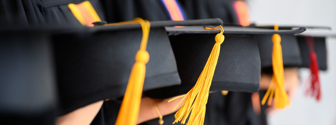 a line of students in graduation gowns holding up their graduation caps with yellow and red tassels