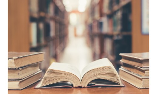 an old and worn book lying open on its spine with piles and aisles of books beside it