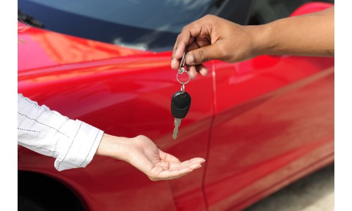 man handing over keys to a woman in front of a red car