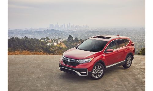 2020 Honda CR-V Hybrid exterior shot with red paint color parked on a cliff with a city skyline in a foggy background