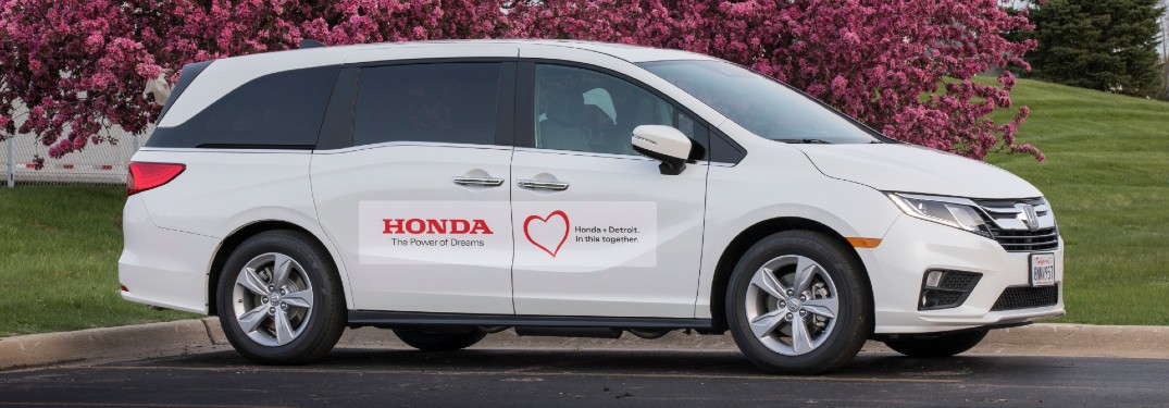 Honda Odyssey minivan modified for COVID-19 testing in Detroit exterior side shot with white paint color parked under a tree with pink and purple flowers