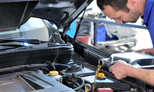 a service team member adding fresh oil to a vehicle under its propped car hood