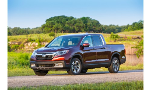 2020 Honda Ridgeline exterior shot with rich red paint color parked on an asphalt road in the country surrounded by tall green grass