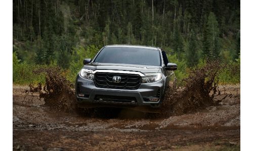 2021 Honda Ridgeline exterior front shot driving through mud as it splashes up with a forest background