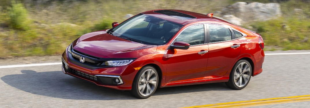 2021 Honda Civic Touring Sedan exterior shot with Molten Lava Pearl paint color driving on a country highway near grassy hills