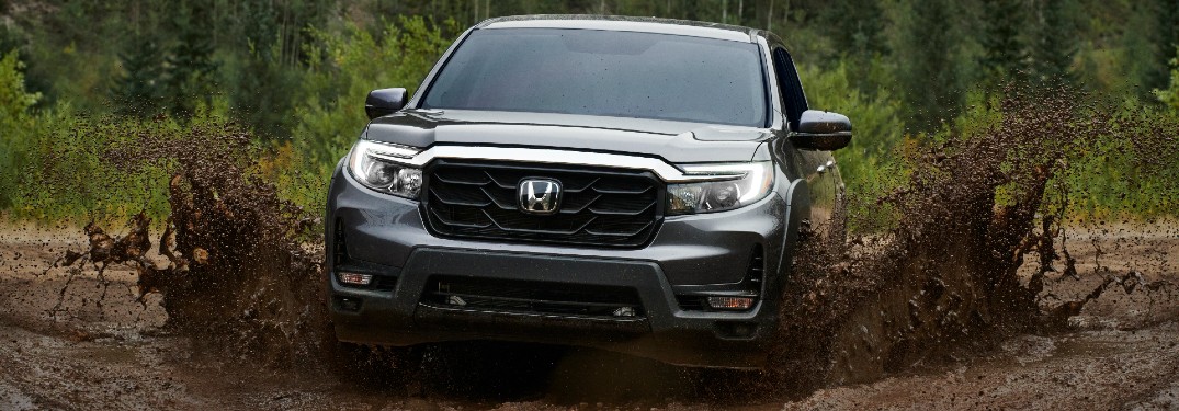 2021 Honda Ridgeline exterior front shot driving through mud as it splashes up with a forest background