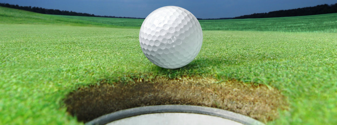 White golf ball coming to a stop at the edge of hole