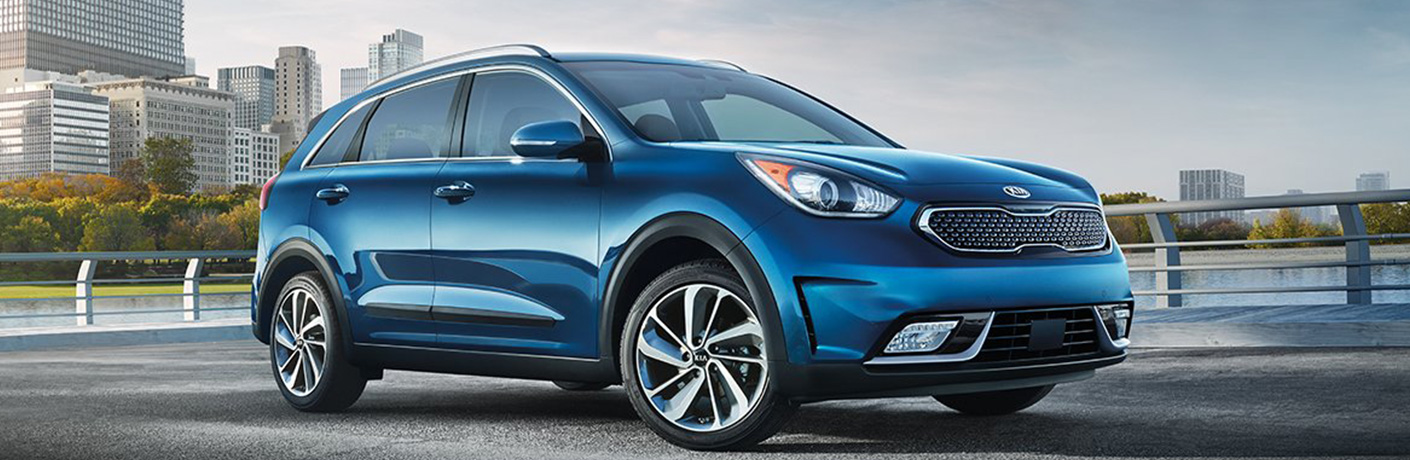 a 2018 blue Kia Niro is parked on the road with a bridge in the back.