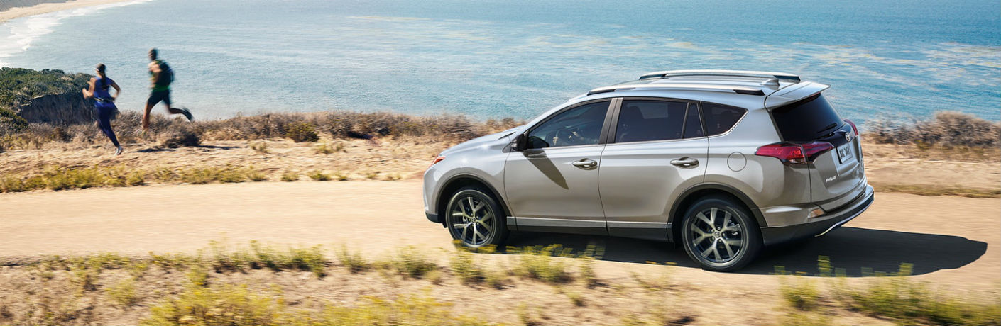 Exterior view of a 2018 Toyota RAV4 parked on a dirt road with ocean in the background