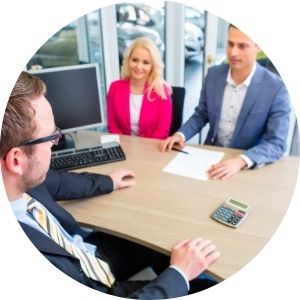 Car Shoppers with Salesman Sitting at a Desk and Signing Paperwork