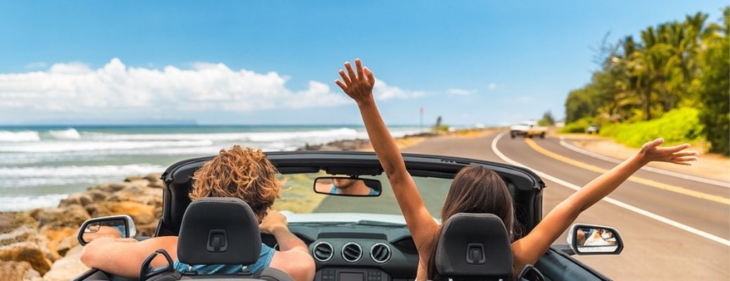 Rear view showing a couple driving in a convertible in a tropical island