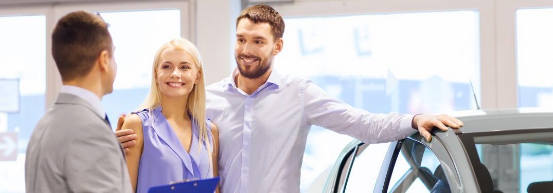 sales man speaking with young couple interested in a new vehicle