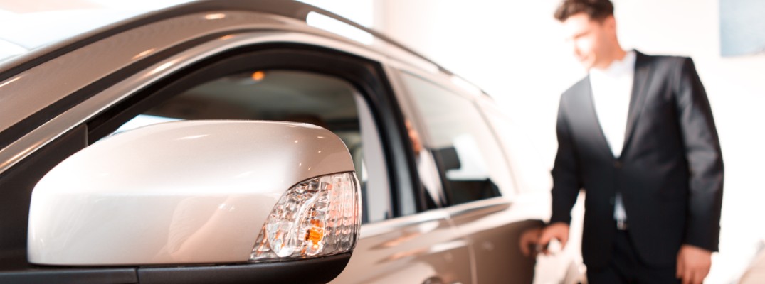 A man standing next to a sedan in the showroom of a dealership