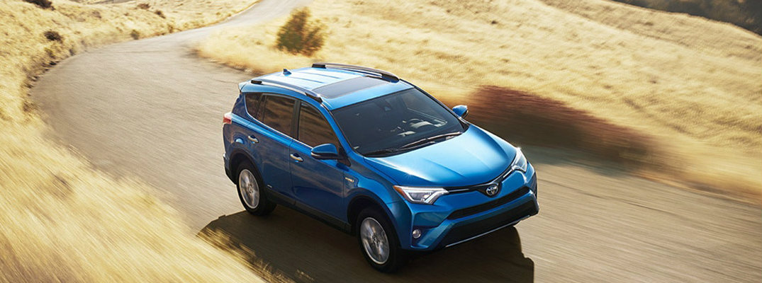 Long shot of blue 2018 Toyota RAV4 Hybrid model driving down grassy road