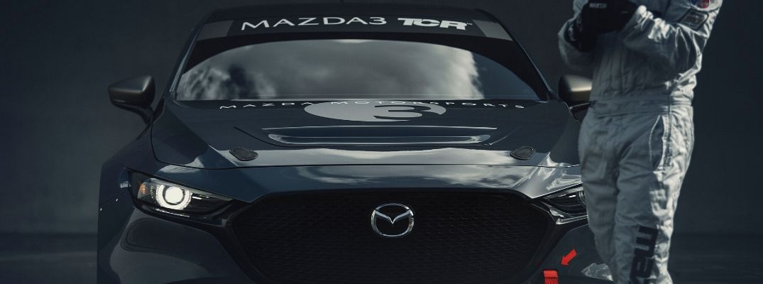 Closeup view of the front of the gray Mazda3 TCR with the driver standing nearby