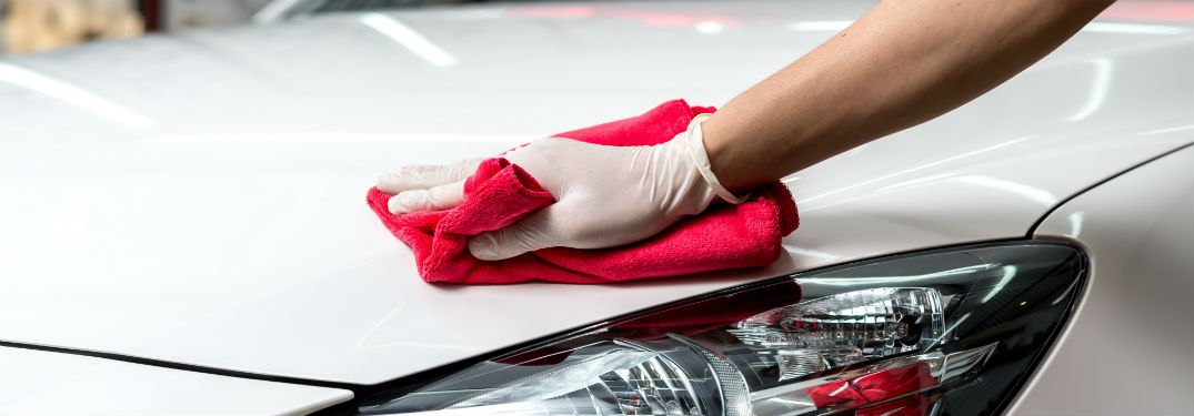 hand with white glove using red rag to wax car