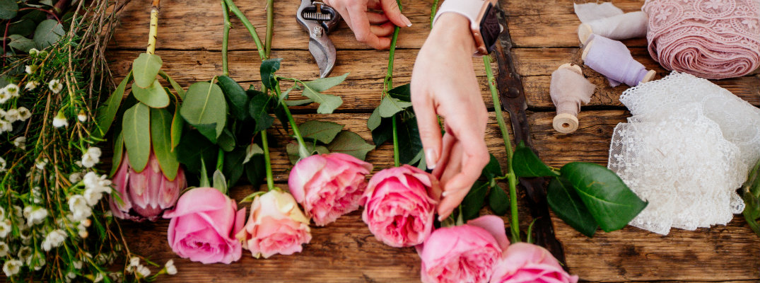 a florist cutting and arranging various flowers on a wooden table top