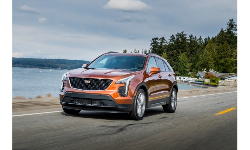 2019 Cadillac XT4 exterior shot with orange paint color driving on a seaside road next to a clear lake and forest