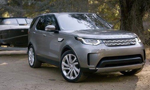 Land Rover Discovery exterior shot with gray paint color towing a boat through a forest