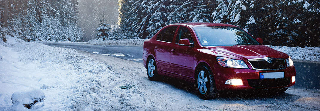 Red car driving on snow and ice covered road in winter