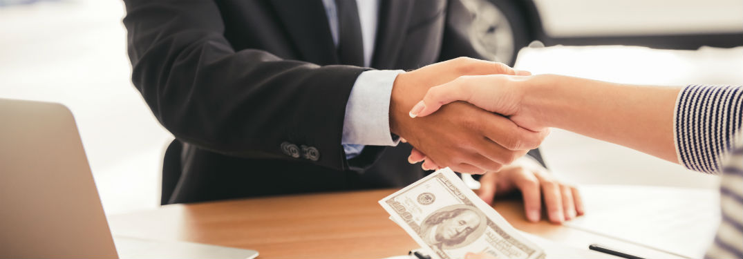Woman shaking mans hand over table with cash