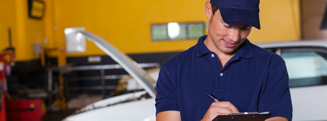 Car mechanic writing on clipboard by vehicle